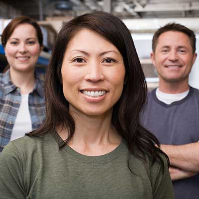 In the photo, 3 people smile - a woman of Asian-American/Pacific Islander heritage standing in front, a man with his arms crossed on her right, and a young woman with brown hair on her left - to represent Clute Wealth Management's financial services for business owners.